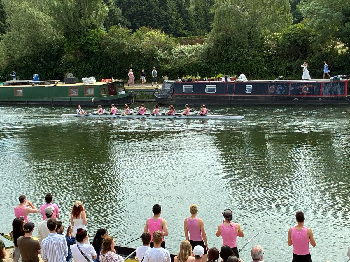 Pembroke College supporters in pink kit watching the women's first VIII race past on the Isis during Summer Eights 2026