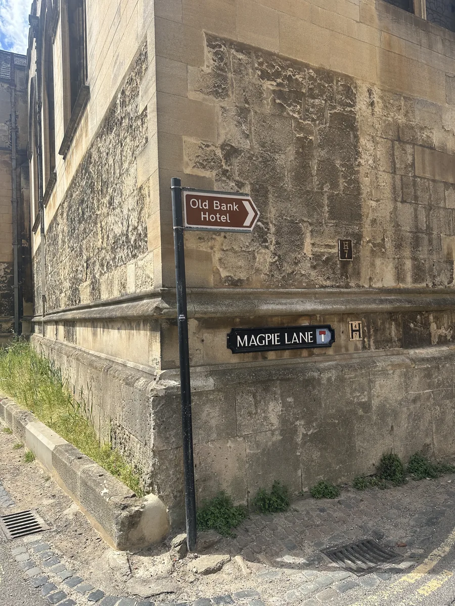 Black-and-white "Magpie Lane" street sign on a stone wall at the High Street end