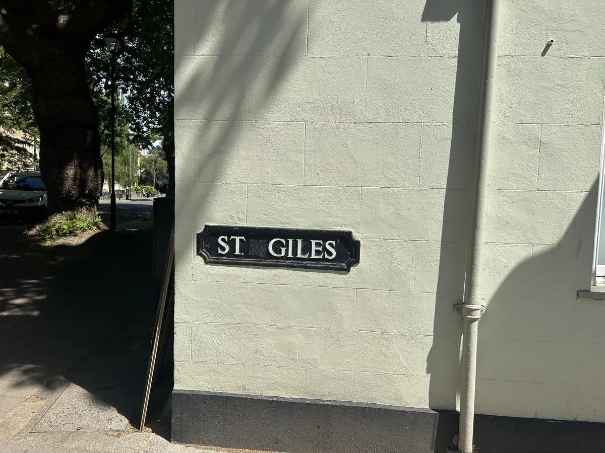 Black-and-white "St Giles'" street sign mounted on a stone wall